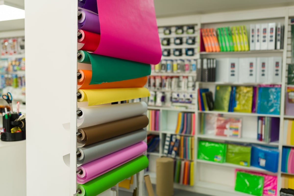 Rollos de papel de colores exhibidos en un anaquel con artículos de papelería